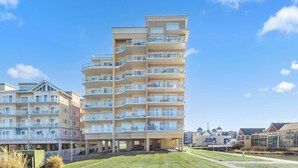 A multi-story residential building with balconies, a parking area, and a grassy courtyard.