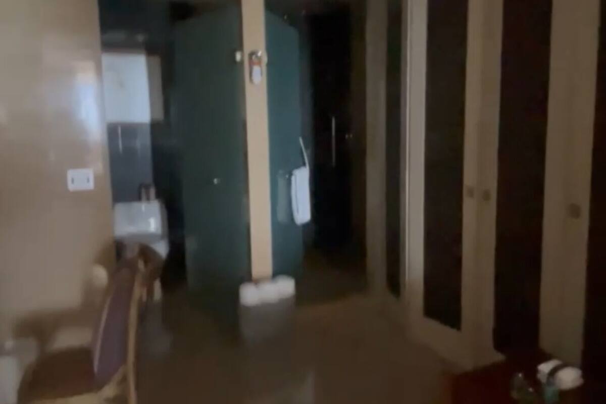 Un couloir faiblement éclairé, avec une chaise, une table sur laquelle se trouvent divers objets, et une porte qui donne sur une autre pièce.