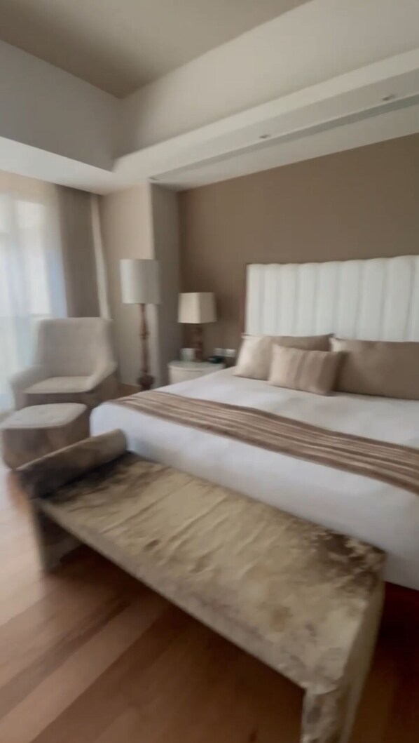 A hotel room with a large bed, a chair, a nightstand, and a bench.