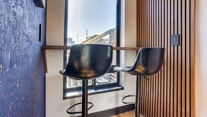 Ein modernes Interieur mit zwei schwarzen Stühlen, einer Wand aus Holzleisten und einem Fenster mit Blick auf Gebäude.