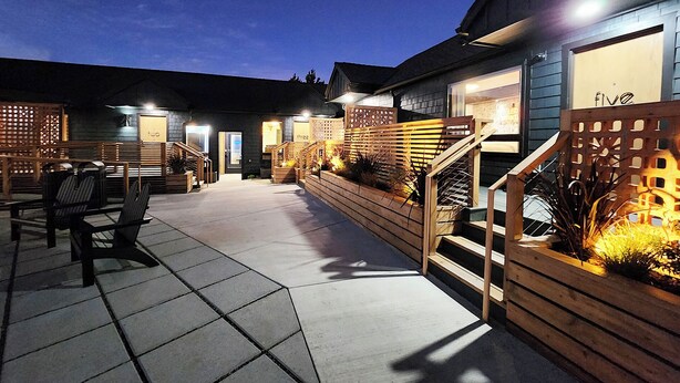 Eine Terrassenfläche mit Sitzgelegenheiten im Freien, Holz-Pflanzkästen mit Pflanzen und eine Treppe zum Hauseingang.
