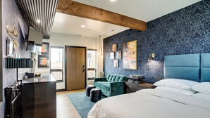 A modern bedroom with a large bed, a blue patterned wall, and a wooden ceiling beam.