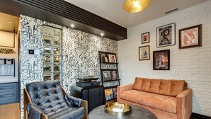 A modern living room with a black leather armchair, a suede sofa, and a coffee table with a tray. There is a record player and a bookshelf with vinyl records. The walls have a black and white abstract wallpaper, and there are framed pictures on the wall. - The Reed @ The Louie Boutique Motel, Private Sauna! Walk to Everything! (Newport)