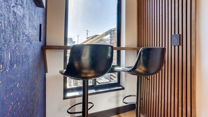 A modern interior with two black bar stools, a large window with a view of buildings, and a wooden slat wall. - The Reed @ The Louie Boutique Motel, Private Sauna! Walk to Everything! (Newport)