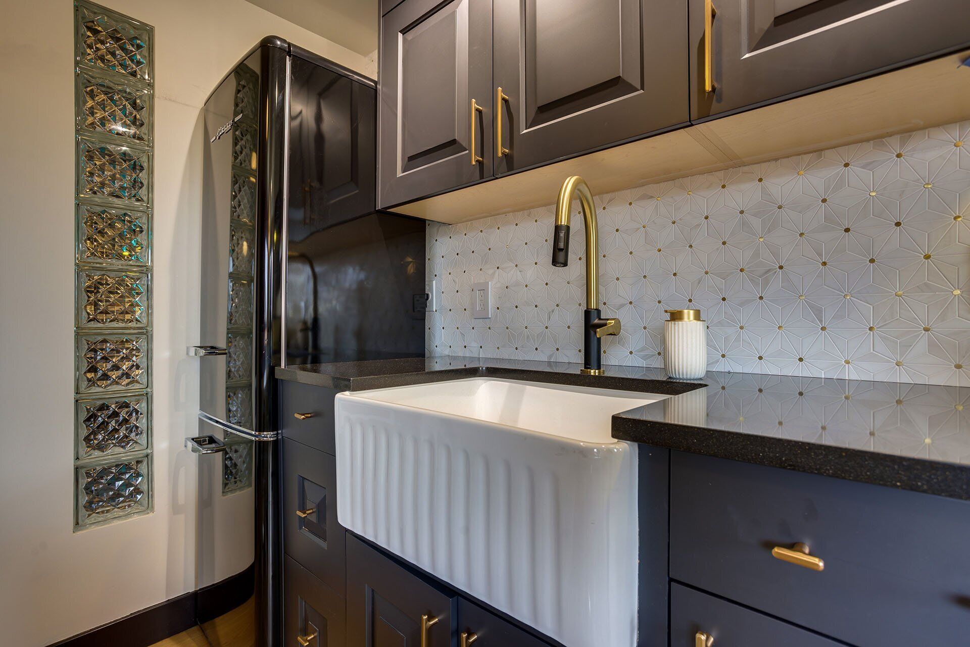 A modern kitchen with dark cabinetry, a white sink, and a geometric backsplash.