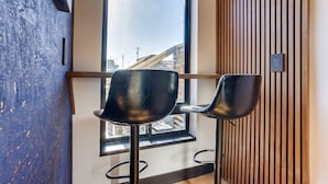 A modern interior with two black bar stools, a large window with a view of buildings, and a wooden slat wall.