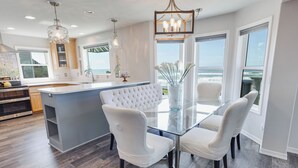 A modern kitchen with a central island, white chairs, and a glass dining table.