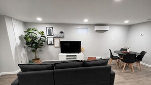 A modern living room with a sofa, TV, dining table, chairs, and a potted plant. - Boutique Studio 10 min. walk to UBS Arena (Elmont)