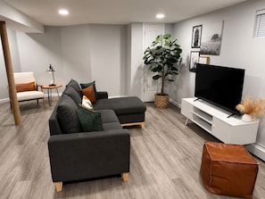 Un salon moderne avec un canapé d’angle, un téléviseur, une plante en pot et une petite table d’appoint.