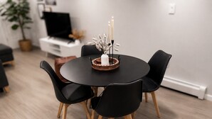A round dining table with four black chairs and a copper base, surrounded by a white wall and a potted plant. - Boutique Studio 10 min. walk to UBS Arena (Elmont)