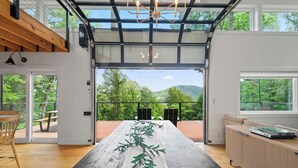 Una habitación amplia con una gran mesa de madera, un banco y vistas a un paisaje verde y exuberante a través de amplios ventanales.