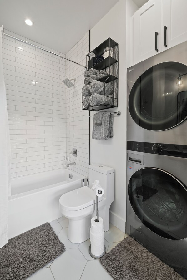 Un baño moderno con ducha de azulejos blancos, inodoro y lavadora integrada.