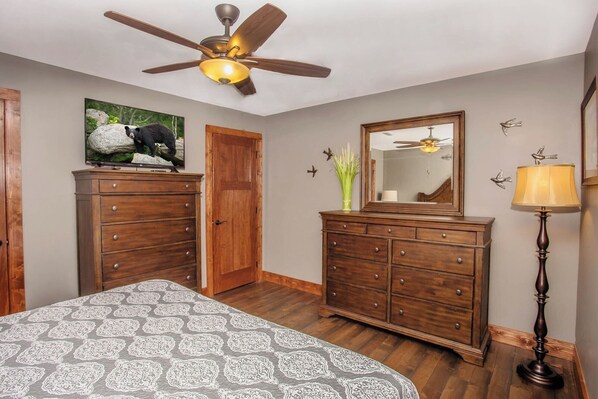 A bedroom with a bed, wooden dresser, ceiling fan, and a mirror.