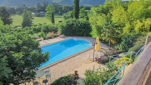 Una piscina rodeada de un patio de piedra y abundante vegetación, con vistas a colinas distantes.