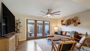Ein Wohnzimmer mit Flachbildfernseher, Ledersofa, Holz-Couchtisch und Deckenventilator.