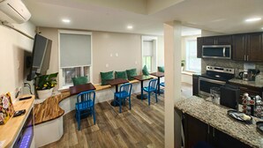 A modern kitchen with a microwave, stove, and granite countertop. There is a dining area with blue chairs and a wooden table. - I Street Capsule Hostel (Washington)