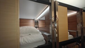 A compact, well-lit train cabin with a single bed, wooden paneling, and a small table. - I Street Capsule Hostel (Washington)