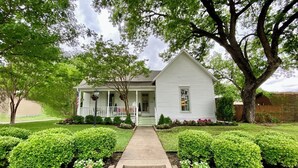 A two-story house with a front porch, a small garden, and a pathway leading to the entrance. - 1883 Boutique Bungalow (McKinney)