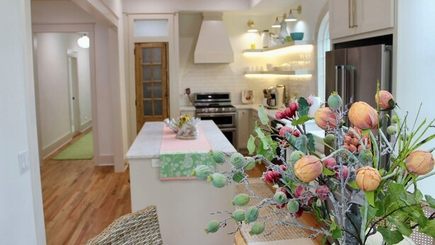 A modern kitchen with white cabinets, a stainless steel refrigerator, and a central island with a green and white patterned tablecloth. - 1883 Boutique Bungalow (McKinney)