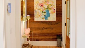 A hallway with wooden flooring, a mirror, a vase with flowers, and a painting on the wall. - 1883 Boutique Bungalow (McKinney)