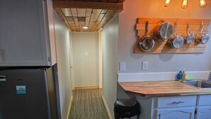 Une cuisine compacte dotée d’un réfrigérateur encastré, d’un plan de travail en bois et d’une étagère à casseroles suspendue.