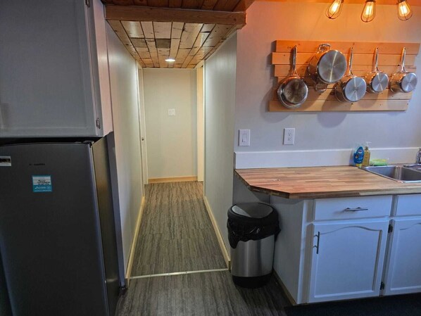 A compact kitchen with a built-in refrigerator, a wooden countertop, and a hanging pot rack. - Charming 2-bedroom house in Nipawin with AC, WiFi, fitness room (Nipawin)