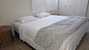 Une chambre à coucher avec un lit, une table de chevet en bois, une armoire et une fenêtre avec des rideaux.