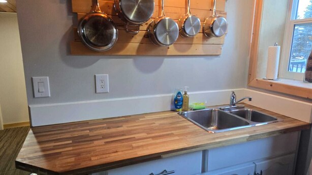Une cuisine avec un plan de travail en bois, un évier à deux bacs et des casseroles accrochées au mur.
