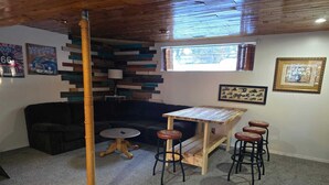 Une pièce chaleureuse avec un plafond en bois, un canapé noir, une petite table ronde et un coin bar avec des tabourets.