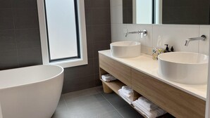 A modern bathroom with two sinks, a bathtub, and a large mirror.