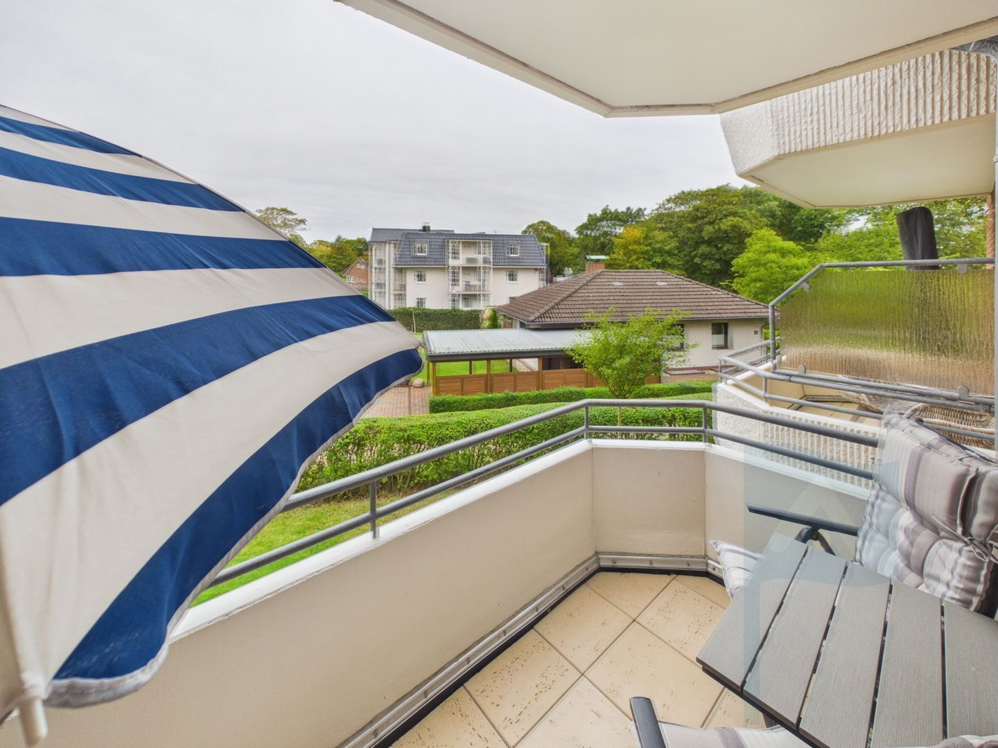 Un balcon donnant sur un quartier résidentiel, avec une rambarde en métal et un sol carrelé.