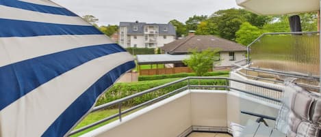 A balcony with a view of a residential area, a metal railing, and a tiled floor.