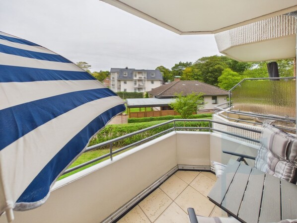A balcony with a view of a residential area, a metal railing, and a tiled floor.