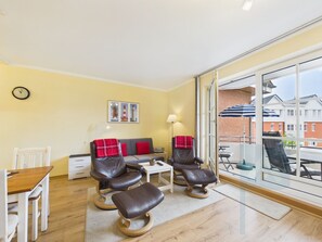 En moderne stue med sofa, to læderstole, et spisebord og et stort vindue med udsigt til bygninger.