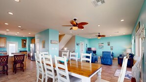 Une cuisine spacieuse dotée d’appareils électroménagers modernes, un coin repas avec des chaises blanches et un salon avec un canapé bleu.