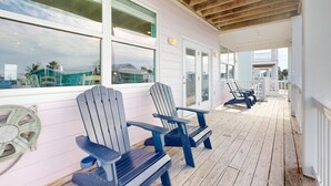 Une terrasse en bois couverte, dotée de chaises Adirondack, de grandes fenêtres et offrant une vue sur l’océan.