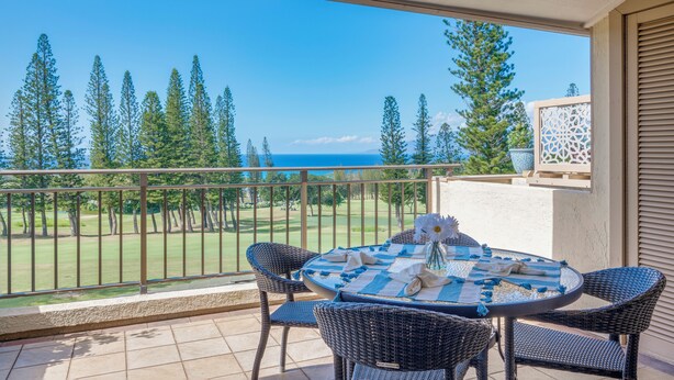 Un balcon avec des fauteuils et une table en osier, offrant une vue sur un terrain de golf et l’océan.