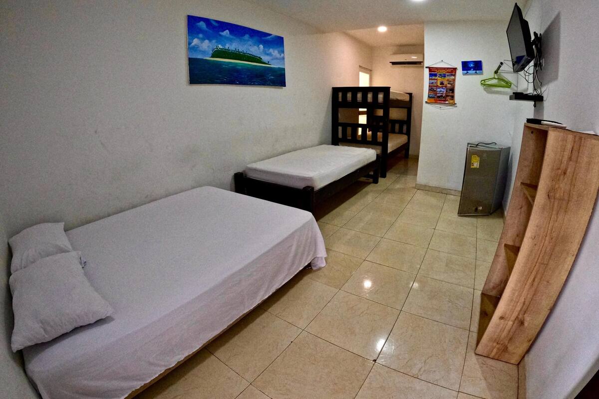 A small, clean room with a single bed, a wooden bench, a TV mounted on the wall, and a poster on the wall.