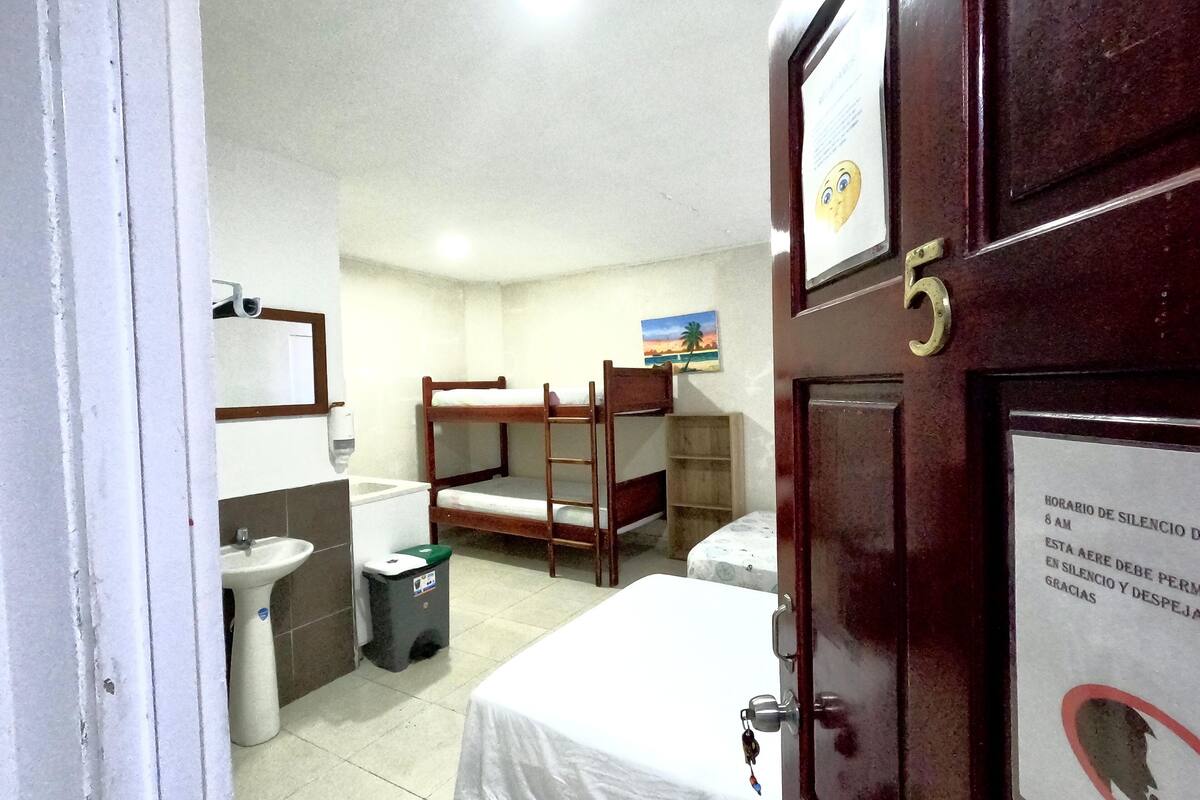 A room with bunk beds, a sink, a trash bin, and a door with a number.