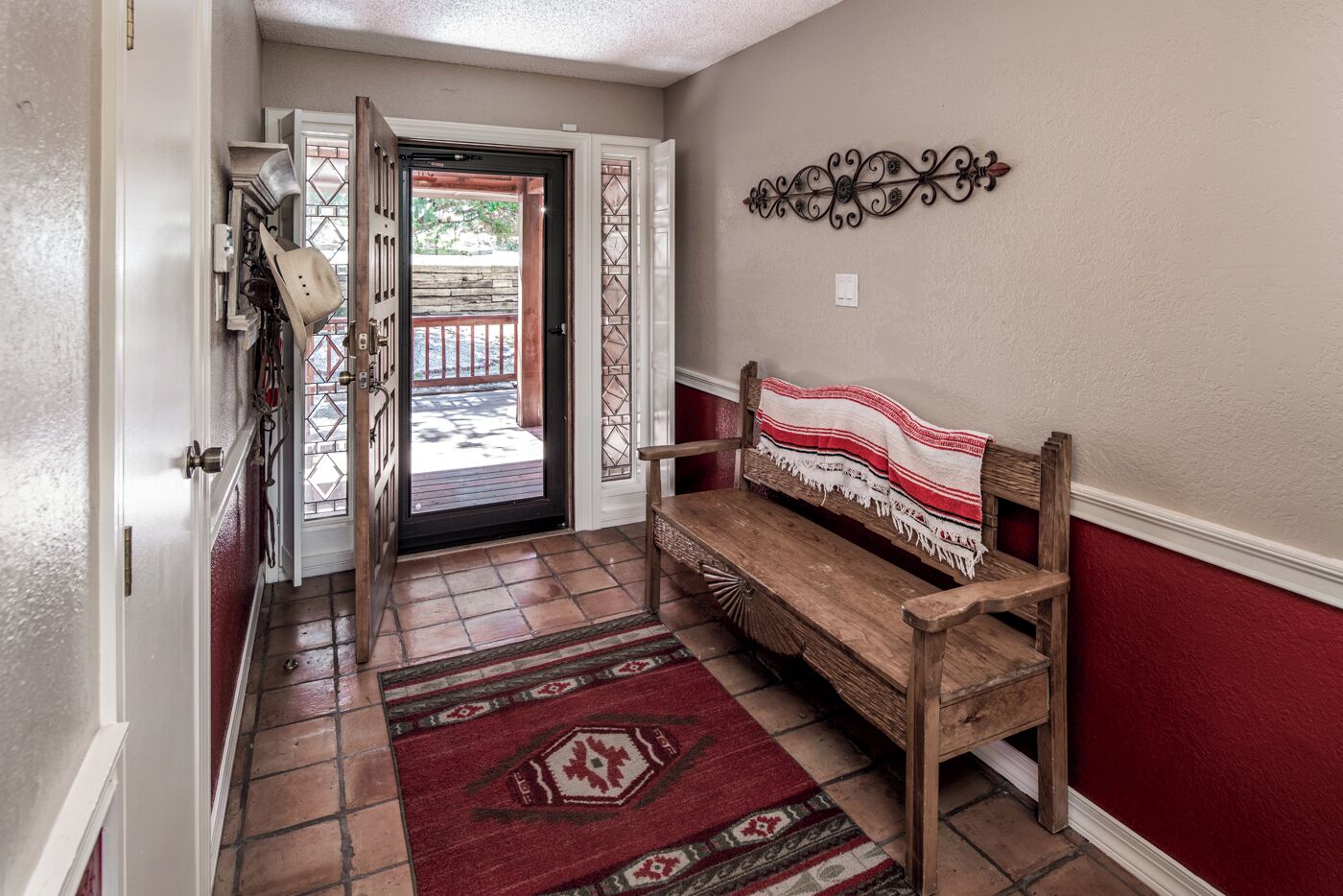 A hallway with a wooden bench, patterned rugs, and a decorative wall piece.