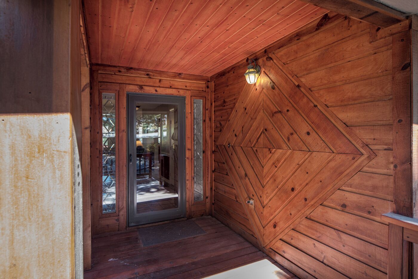 A wooden interior with a door leading to an outdoor area, a wooden floor, and a wall with a geometric pattern.