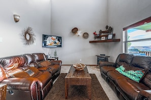 A living room with two leather sofas, a coffee table, decorative wall art, and a television. - Love Prescription (Ruidoso)