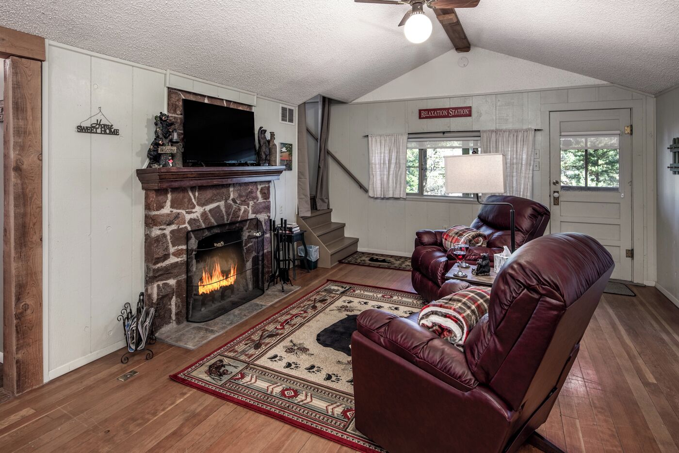 A cozy living room with a stone fireplace, leather sofa, and a staircase leading to another level.