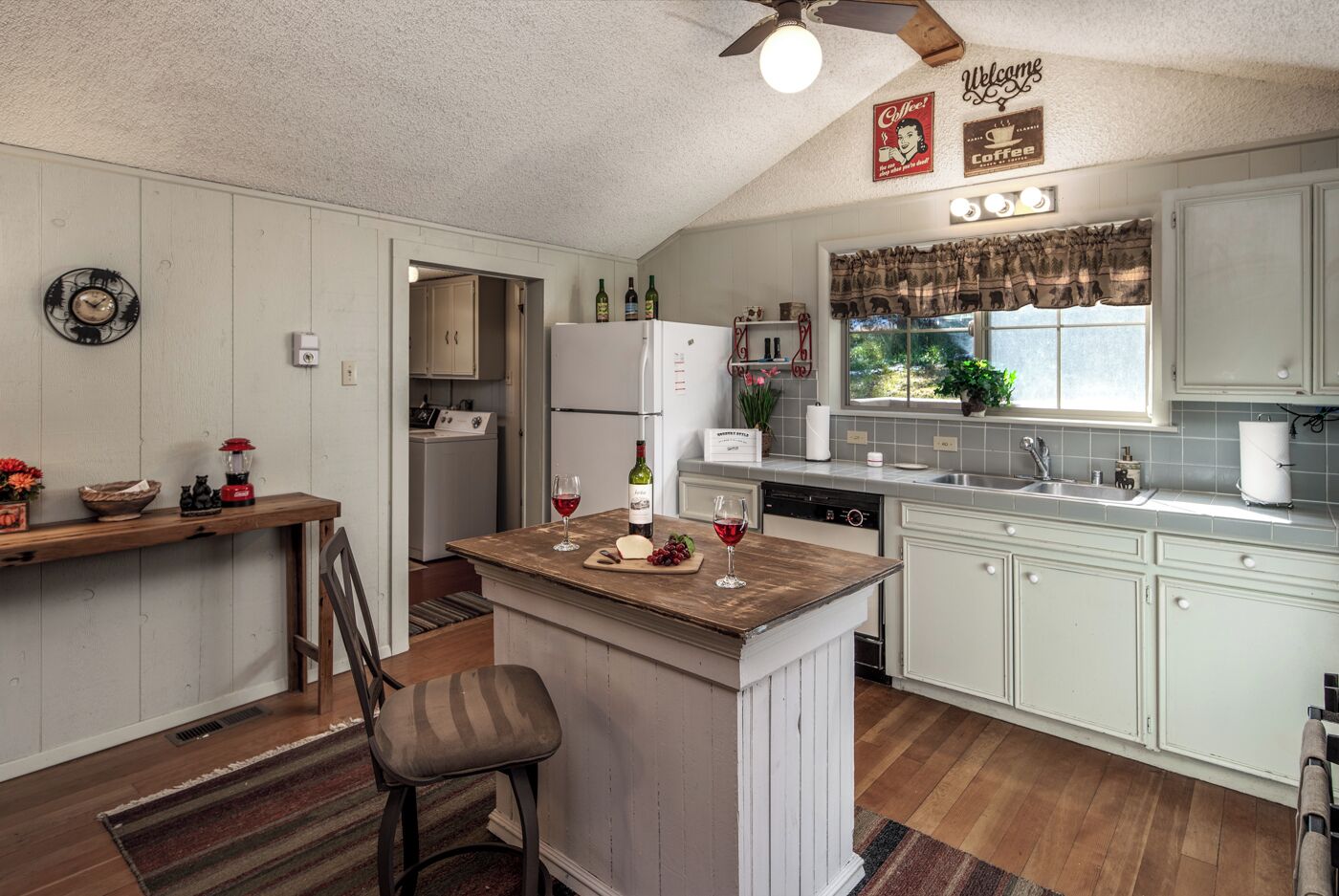 A compact kitchen with a central island, a refrigerator, a dishwasher, and a window with curtains.
