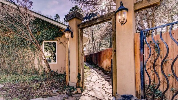 A stone pathway leading to a gated entrance with a wooden archway and metal gate. - Riverside Retreat (Ruidoso)