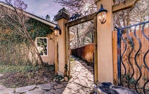 A stone pathway leading to a gated entrance with a wooden archway and metal gate. - Riverside Retreat (Ruidoso)