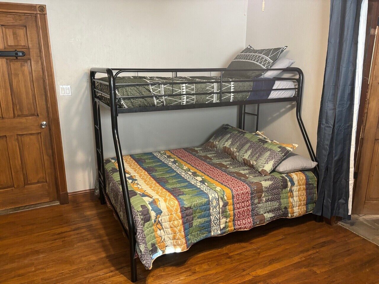 A bunk bed with a colorful quilt, a wooden door, and a curtain.