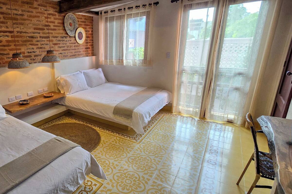 A hotel room with two beds, a brick wall, a window with curtains, and a patterned floor.