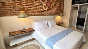 A bedroom with a brick wall, a bed with white bedding, two bedside lamps, and a wooden nightstand. - Hotel Casa de la Acequia (Santa Marta)