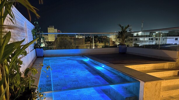 A rooftop pool with blue lighting, surrounded by plants and a cityscape view. - Hotel Casa de la Acequia (Santa Marta)